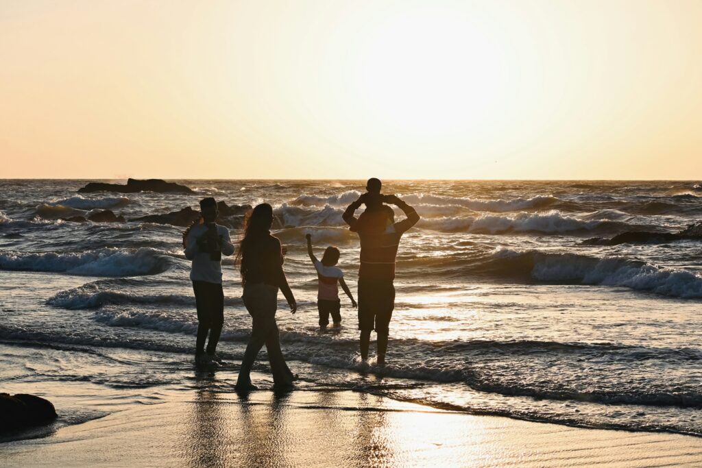Família caminhando na beira do mar ao pôr do sol