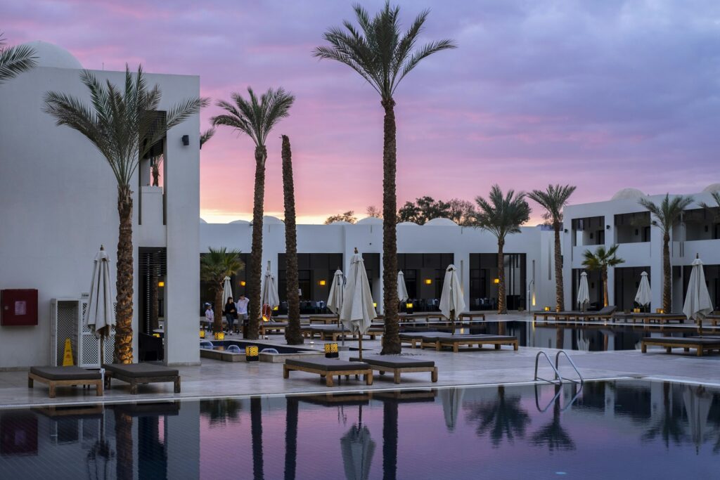 Piscina de resort cercada por palmeiras ao entardecer